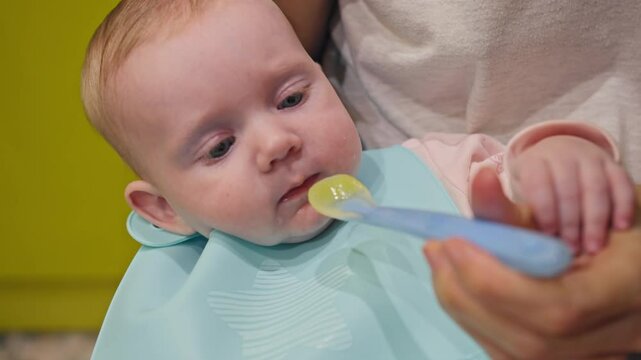Baby girl try puree food from spoon, Mom feeds baby new food and weaning