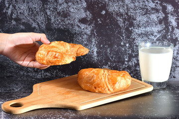 A woman's hand holds a glass of milk and a croissant is placed on it. Croissants and milk, homemade morning dayly breakfast on dark wall texture with copy space.