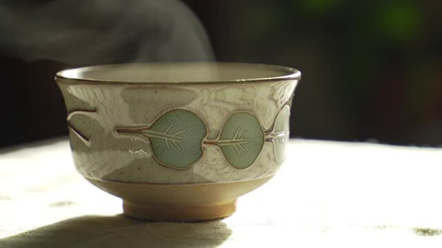 Una taza de t&eacute; de cer&aacute;mica hecha a mano sobre una mesa cubierta de lino con la suave luz de la ventana de la ma&ntilde;ana, el vapor se eleva en delicados remolinos,