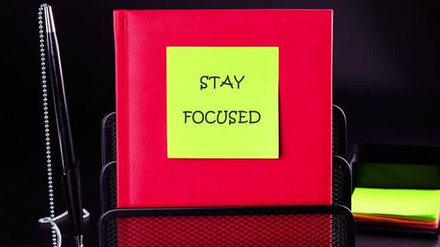 A bright green sticker with text animation Concept word Stay Focused is placed on a red notebook, which emphasizes encouragement for initiative in a professional work environment