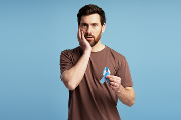 Worried man holding blue ribbon and touching face with hand