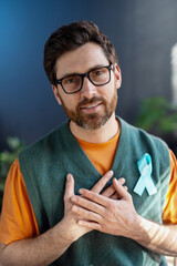 Man showing light blue ribbon supporting prostate cancer awareness, placing hands on chest
