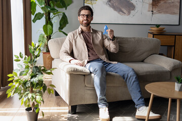 Man smiling and holding a paper airplane at home