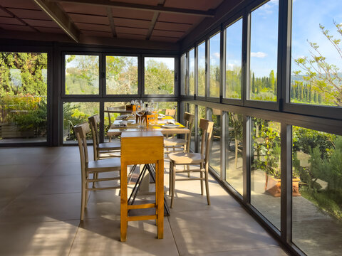sunlit modern open-air restaurant interior with panoramic windows surrounded by Tuscan landscape with cypresses, olive groves and vineyards. dining
