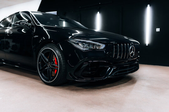 Front-side view of black Mercedes Benz CLA 45 S AMG C118 in detailing studio. Aggressive design, red brake calipers, and LED headlights under modern lighting. Marketing materials, advert or press.