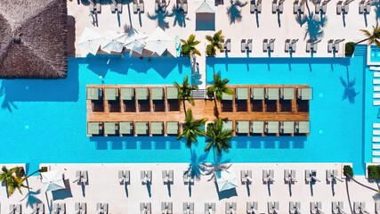 Aerial view of hotel swimming pool with sun loungers and umbrellas around. Beautiful sunny summer day by the pool with blue water. Summer activities. View from a flying drone on a luxury beach.