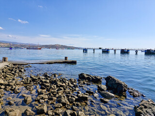 Scenic harbor view with a distant dock, fishing boats, and rocky shores where boats are moored