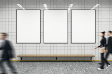 Three vertical blank posters in black frames on a tiled wall above a wooden bench, people walking...