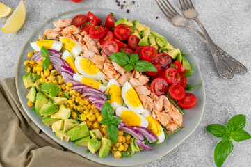 Salmon salad with avocado, boiled eggs, sweet corn, tomatoes, lettuce and red onion on concrete background. Healthy food. Top view.