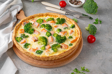 Homemade tart or quiche with salmon, broccoli, cheese and cream filling on a gray stone background. Healthy food. Selective focus.