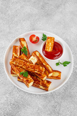 Fried halloumi cheese sticks with tomato sauce on a white plate on a concrete background.