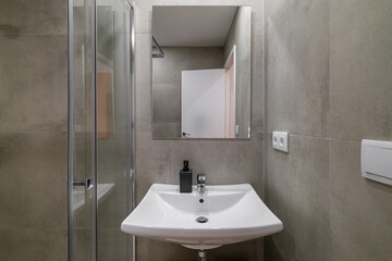 Modern bathroom space with gray stone walls glass shower and square sink basin under mirror