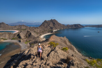 A breathtaking elevated view reveals a rugged coastline of Padar Island with turquoise waters, as a woman hiker embraces natures beauty and captures the essence of exploration, Komodo, Indonesia