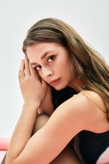 Naklejka premium Captivating young woman with flowing hair gazes thoughtfully against a soft backdrop