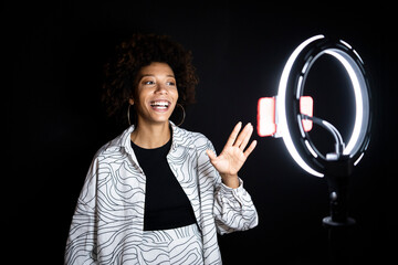Fashionable young woman gesturing while vlogging against black background