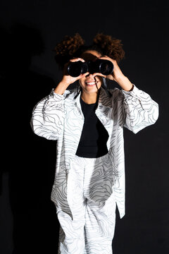 Fashionable woman holding binocular against black background