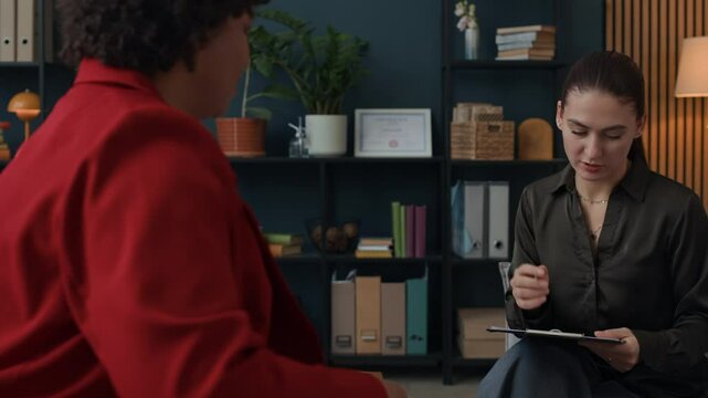 Medium shot of female African American psychologist asking young Caucasian woman to pass test during therapy session