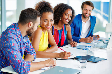 Diverse team of smiling professionals collaborating at modern office workspace. Colorful business meeting with multiethnic colleagues engaged in creative project planning. Productive partnership