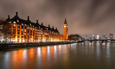 Fototapeta premium Night view of the Houses of Parliament, London, with the River Thames reflecting the city lights. Possible use Stock photo for travel brochures, city guides, or online travel advertising