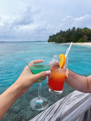 Hands holding colorful summer cocktails near ocean. Tropical vacation, or honemoon celebration. Beach party