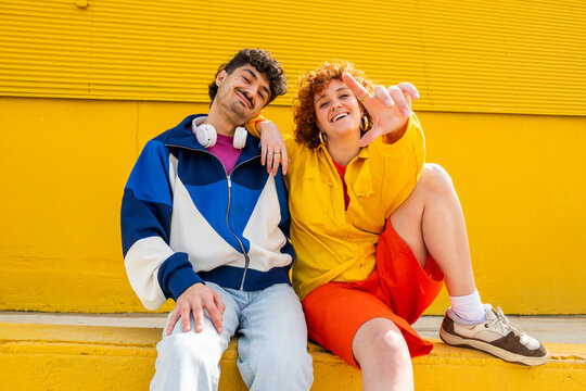 Friends sitting against a yellow background wearing urban clothing and smiling at the camera