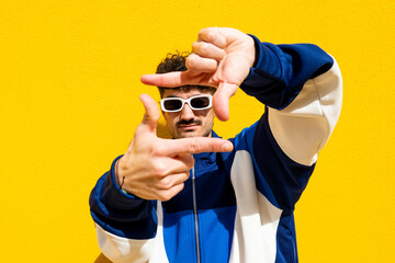 Man in urban clothing posing with hand frame gesture against a yellow background