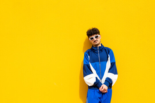 Young man in urban clothing and sunglasses posing against a yellow background on a sunny day