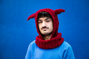Young man in urban clothing with a red knit hat against a blue background
