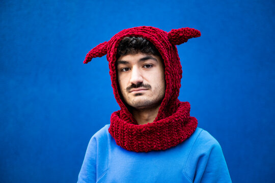 Young man in urban clothing with a red knit hat against a blue background