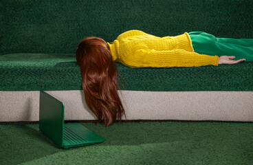 Red-haired woman lying on a couch at home with a laptop, appearing tired and resting.