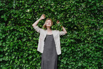 Woman standing against a wall of green leaves, embodying mental health and work-life balance