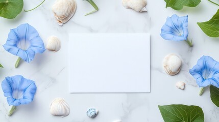 A white card with a blue flower on it sits on a table with shells and flowers. The card is empty.