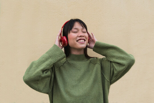 Woman in green sweater enjoying music with headphones on a street