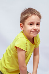 Naklejka premium Smiling young boy with short brown hair wearing a bright yellow t-shirt, leaning slightly forward. His expression is playful and curious, with a dimple visible on his cheek