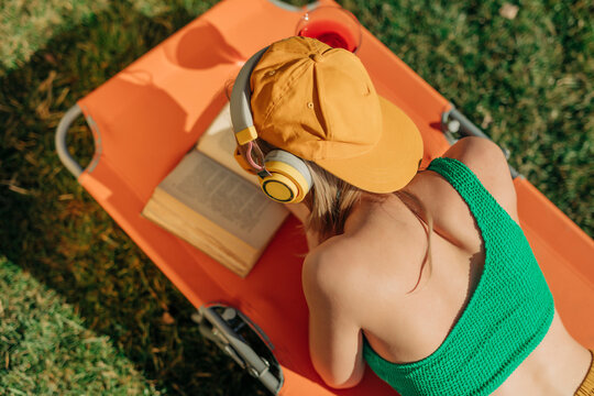 Person relaxing on a sun lounger in the backyard, reading a book and listening to music on headphones