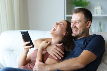 Funny couple laughing together checking phone content at home