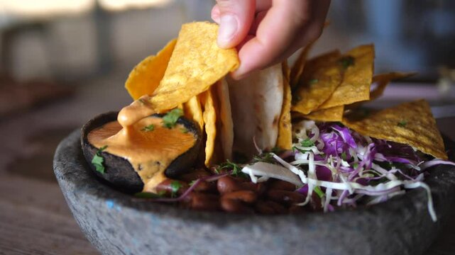 Creamy cheese sauce cascading over tortilla chips, complemented by beans and red cabbage in rustic stone bowl, capturing authentic mexican dining experience with vibrant flavors and textures