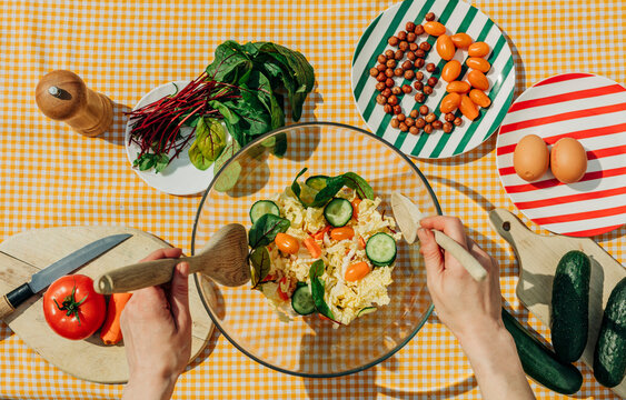 Woman preparing a summer salad with fresh vegetables and ingredients on a gingham tablecloth