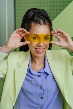Young woman in a yellow blazer holding a yellow filter in front of her eyes