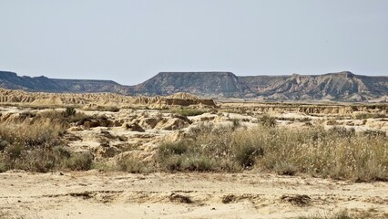 Panoramic view of semi-desert Bardenas Reales in Navarre, Spain. The terrain is arid, rocky with sparse vegetation. The eroded hills with stratified layers of earth. Dry grasses and scattered shrubs. 