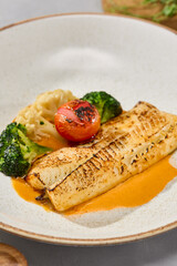 Coalfish fillet with cod, vegetables, and bisque sauce plated on neutral background, natural lighting, minimalistic style
