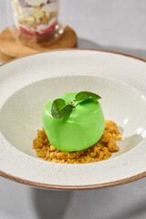Glossy apple-shaped mousse cake on textured crumble, studio lighting, vibrant color palette