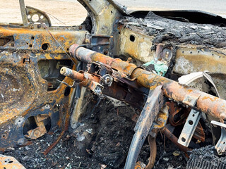 Burned steering column and dashboard frame from a car showing rusted metal structure, melted...