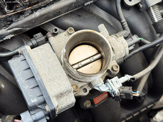 Close-up of a car engine throttle body showing the butterfly valve, electronic actuator, and...