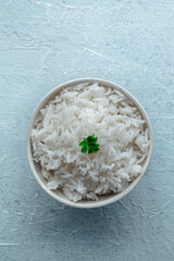 White rice, cooked. A bowl of boiled long grain rice, a simple side dish, with fresh parsley leaves, top shot