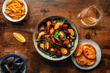 Mussels with French fries, white wine, lemon, and toasted bread, moules frites, shot from above on a wooden table