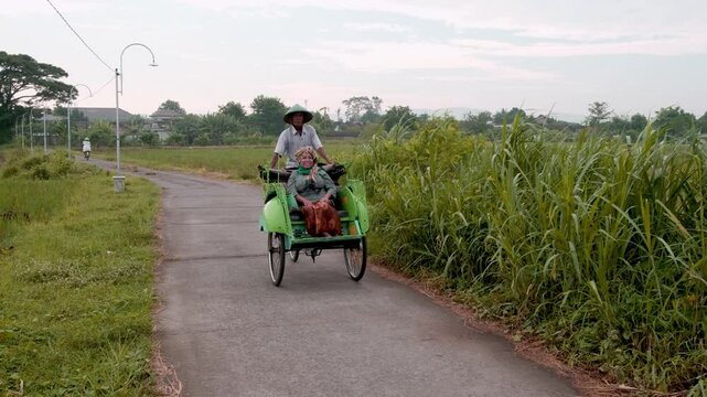 Javanese becak driver transporting passenger on rural road