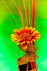 Rotgelbe Gerbera in Ziervase mit Dekoschmetterling Hintergrund lila bis blau