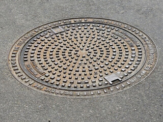 Detailed circular metal manhole cover on pavement with geometric pattern