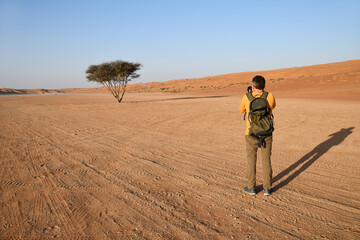 Man takes photo of acacia tree. Wahiba Sands. Sultanate of Oman